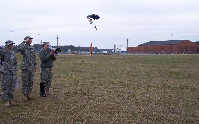Past JROTC Raven Battalion Commander Maddie Crimmons, right, of Millsboro sings the national anthem through a bullhorn while U.S. Naval Academy Midshipman Second Class Brian Holloway brings down the American flag attached to his parachute. Saluting the flag are C/CPT Bradley Gordon of Milton, left, and C/LTC Dylan Varrato of Georgetown. SOURCE SUBMITTED